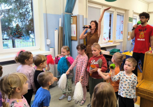 Pani z mikrofonem śpiewa, a dzieci grają na instrumentach